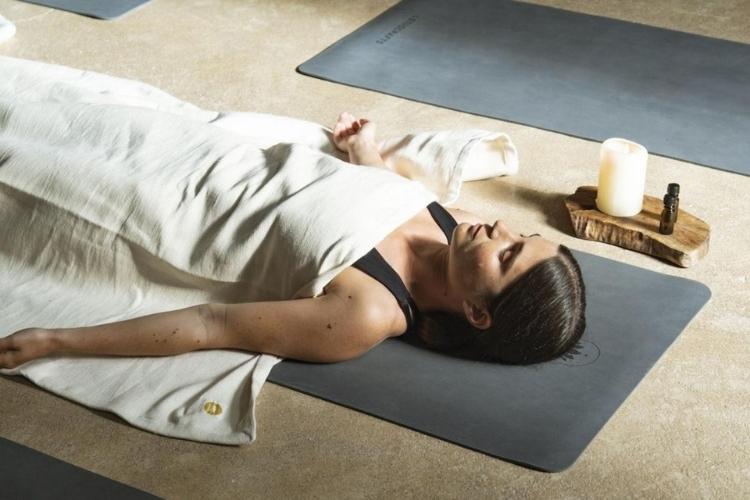 Mangolds Yoga-Online Shop - Dunkelhaarige Frau liegt zugedeckt auf einer Yogamatte und macht Shavasana