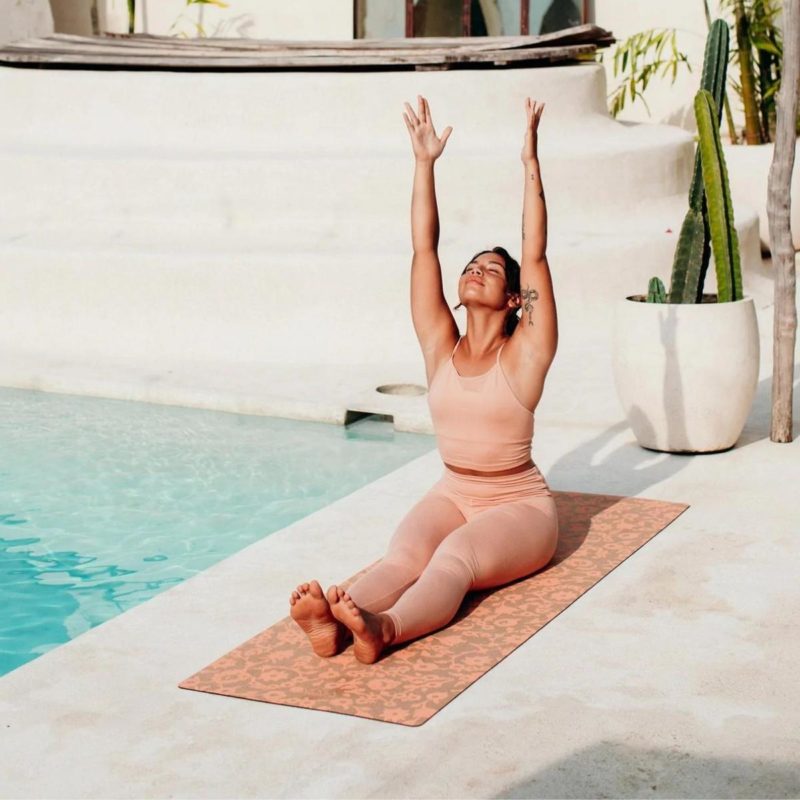 Frau macht Yogapose auf Yogamatte neben dem Pool