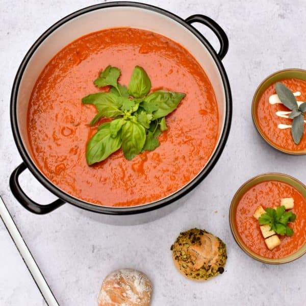 Topf mit Tomatensuppe daneben Suppenschüsseln und Gebäck